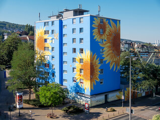 blue skyscraper painted with oversized sunflower blossoms in Wuppertal Oberbarmen, in the background is the suspension railroad