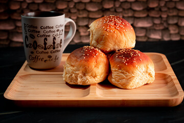 bread buns with sesame on wooden plate dark table stone wall, with white coffee rate