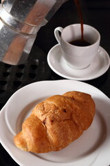 Croissant and pouring coffee from moka pot into cup