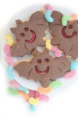 Halloween cookies in shape of a bat filled with marmalade on a plate with worm candies isolated on white background