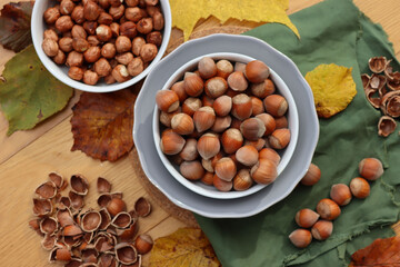 Whole hazenuts in a bowl with cracked hazenuts and autumnal leaves on wooden background