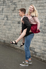 Happy man giving piggyback ride to his girlfriend and laughing near gray wall