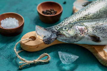 Two fish, raw trout with spices and ice on a cutting Board on a turquoise background. close-up