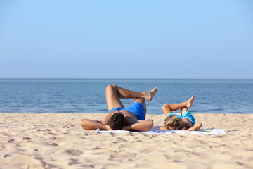 Fototapeta na wymiar Father and son lying on sandy beach near sea. Summer holidays with family