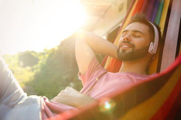 Young man listening to music in hammock near motorhome outdoors on sunny day
