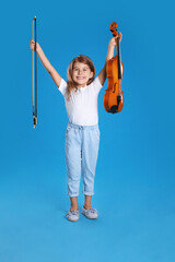 Little girl with violin and bow on light blue background
