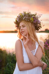 Young woman wearing wreath made of beautiful flowers outdoors at sunset