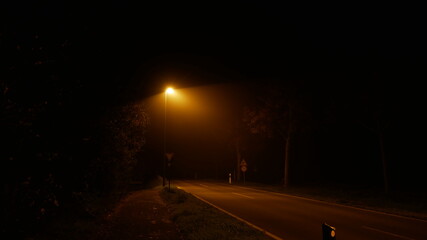 Einsame Landstraße in der Nacht im Nebel mit einer fahlen Straßenlaterne (Natriumdampf) erzeugt...