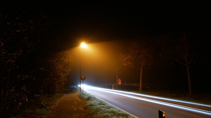 Einsame Landstraße in der Nacht im Nebel mit einer fahlen Straßenlaterne (Natriumdampf) und...