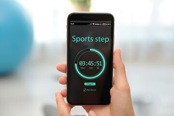 Young woman using fitness app on smartphone indoors, closeup