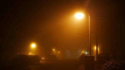 Dorfstraße in der Nacht im Nebel und Laternen beleuchten die Strasse auf eine unheimliche und...