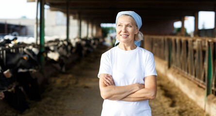 Portrait of smiling mature female farmer standing near cows at the cow farm
