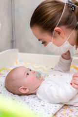 the baby tries to tear off the protective mask from her mother s face during the coronovirus and covid-19 pandemic.