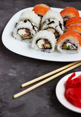sushi rolls on a white plate on a black background with pickled ginger