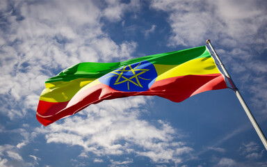 Beautiful national state flag of Ethiopia fluttering at sky background. Low angle close-up Ethiopia flag 3D artwork. - obrazy, fototapety, plakaty