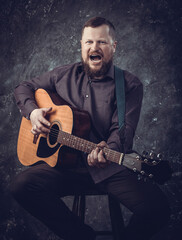 Mature musician plays acoustic guitar emotional studio portrait.