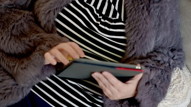 Frau in einer Kaninchenfell Jacke arbeitet mit einem Tablet PC im Homeoffice  