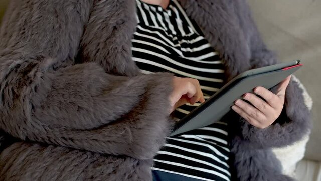 Frau in einer Kaninchenfell Jacke arbeitet mit einem Tablet PC im Homeoffice  