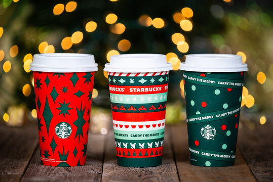 Dallas, Texas - November 12, 2020: Starbucks popular holiday beverage, served in the new 2020 designed holiday cups. Displayed on rustic wooden table. Christmas tree lights bokeh background.