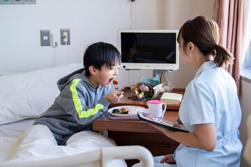 女性看護師の付き添いで自分で食事を食べる入院中の男の子