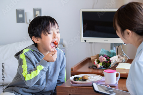 女性看護師の付き添いで自分で食事を食べる入院中の男の子 Wall Mural Monet