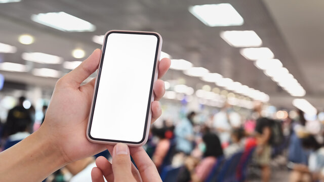 Cropped shot of man hands holding mobile phone with white screen on blured airport terminal background.