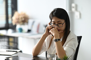 A stressed young office worker sitting at desk while talking on the phone and feeling stress from work in the office.
