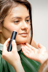 Makeup artist applying cream blush stick foundation on cheek of young caucasian woman