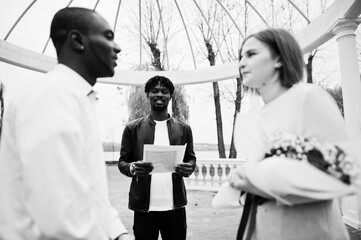 Obraz premium Wedding engagement ceremony with pastor. Happy multiethnic couple in love story. Relationships of african man and white european woman.