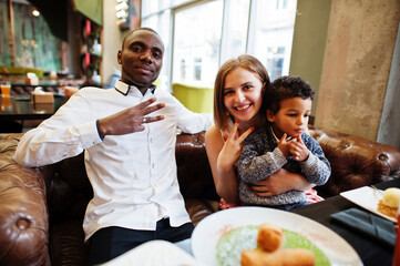 Happy multiethnic family with boy kid spend time at restaurant. Relationships of african man and white european woman.
