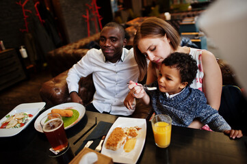Happy multiethnic family with boy kid spend time at restaurant. Relationships of african man and white european woman.