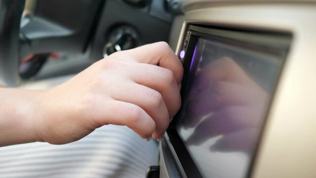 Young woman hand with elegant manicure of purple colour rotates grey button at coloured dashboard display in new automobile close view