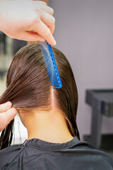 Back view of hairdresser hands parting long hair of young woman in hair salon