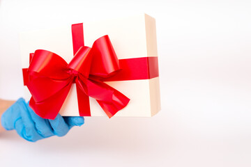 Holiday gift.Hand wearing meidical gloves holding gift box with red ribbon.white background.