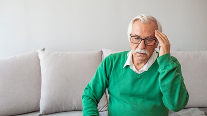 A Distraught Senior Man Suffering From a Migraine While Sitting on the sofa in the Living Room. Cropped shot of a senior man suffering from a headache. 