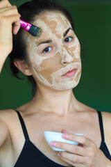 young brunette woman with a clay homemade mask on her face