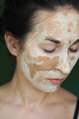 young brunette woman with a clay homemade mask on her face with her eyes closed
