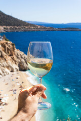 A glass of white wine in a man's hand. Wine against the backdrop of the sea coast and a sunny summer beach. Wine tasting and relaxation at the resort