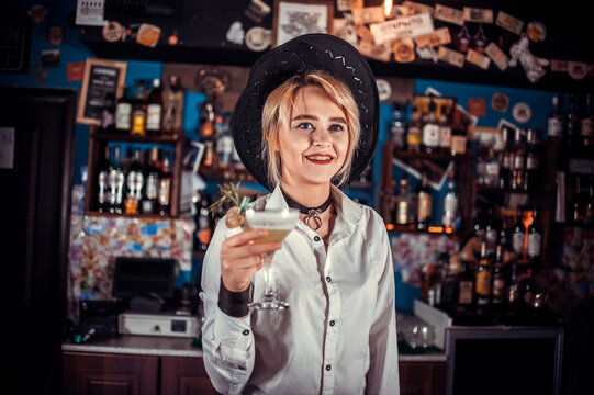 Confident woman barman adds ingredients to a cocktail in pub