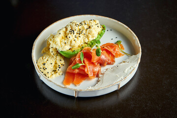 Perfect breakfast - scrambled eggs with salmon, avocado and cream cheese in a white plate. Selective focus