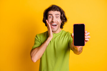 Portrait photo of amazed blurred man showing screen smartphone blank space touching cheek isolated on bright yellow color background