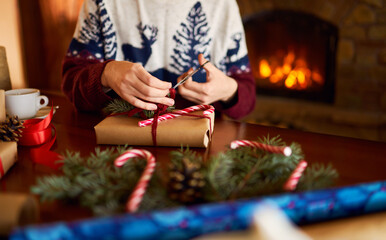  Men's hands hold Christmas present.  Man using red ribbon, green fir tree twig to create Christmas gift. Wintar holiday. 