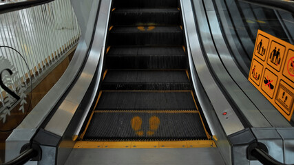 staircase escolator in a shopping center with a footprint sign for keeping a social distance