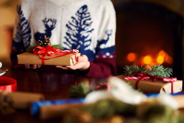  Men's hands hold Christmas present.  Man using red ribbon, green fir tree twig to create Christmas gift. Wintar holiday. 