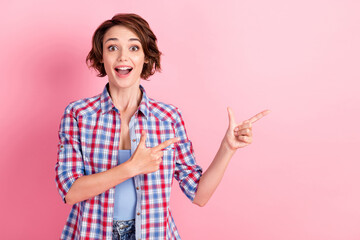 Photo of surprised funny young woman wear checkered shirt pointing empty space isolated pink color background