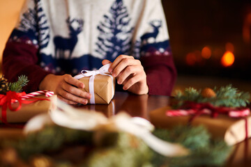  Men's hands hold Christmas present.  Man using red ribbon, green fir tree twig to create Christmas gift. Wintar holiday. 