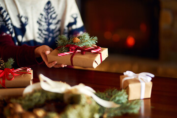  Men's hands hold Christmas present.  Man using red ribbon, green fir tree twig to create Christmas gift. Wintar holiday. 