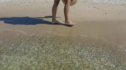 Woman walking on sandy beach washed by sea waves, slow motion effect. Camera tracking and moving backward