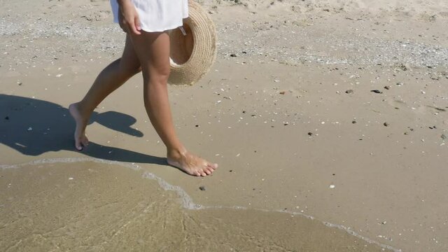 Woman walking on sandy beach washed by sea waves, slow motion effect. Camera tracking