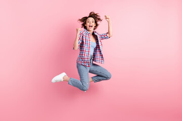 Full length photo of cute lucky young lady dressed plaid shirt jumping high hands arms fists isolated pink color background